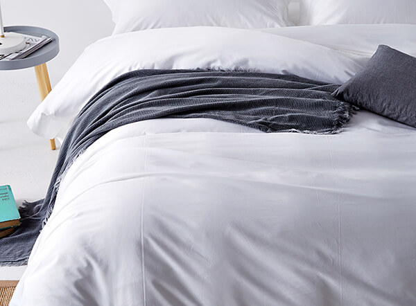 White bed linen set with a grey throw on a made bed