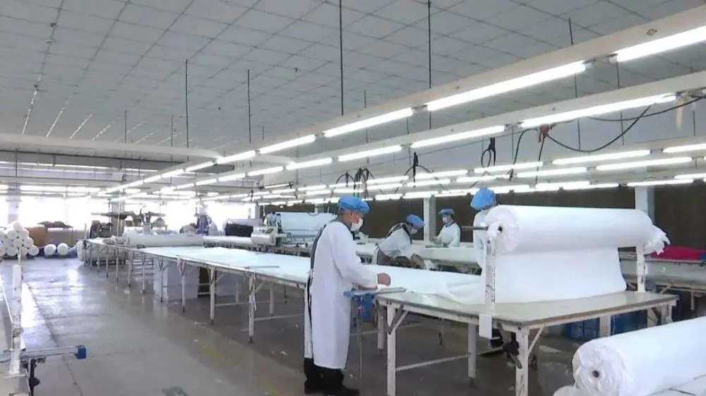 Workers inspecting and rolling finished fabric on a production line