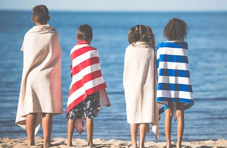 Children wrapped in striped beach towels on the sand facing the sea